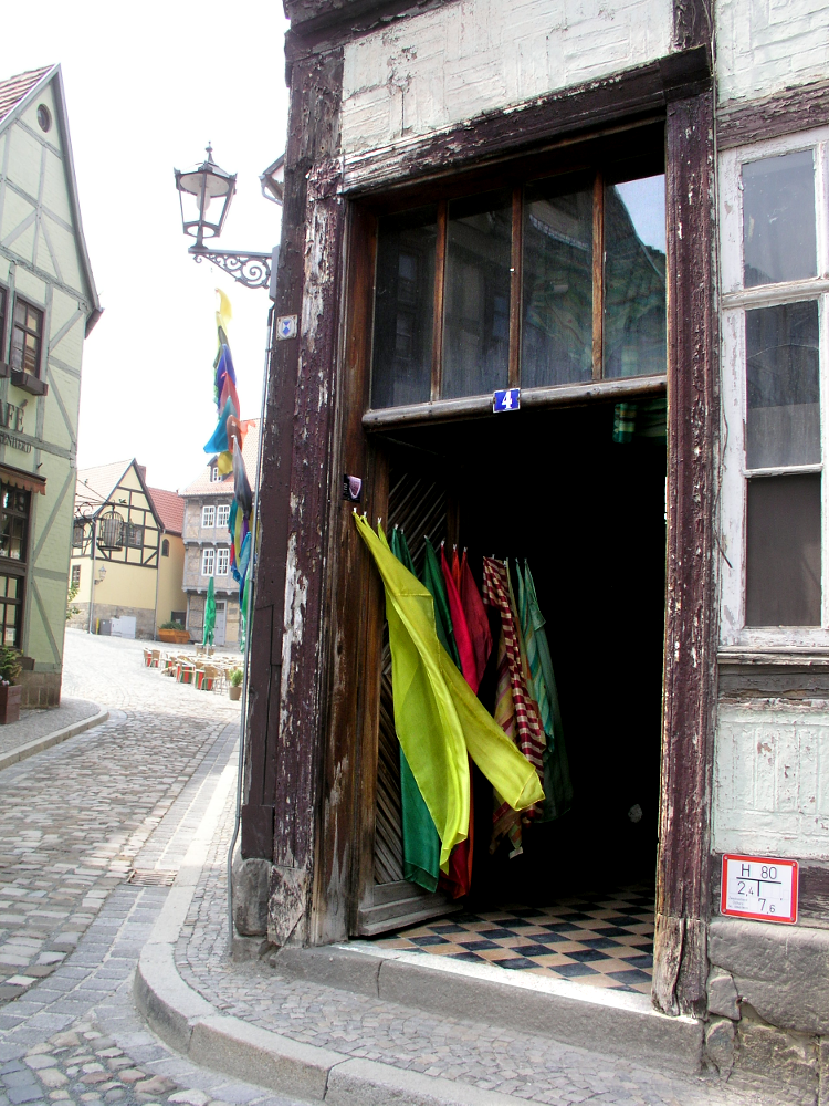 Aus dem Eingang eines nicht sanierten Fachwerkhauses winken bunte Seidentücher hervor.
