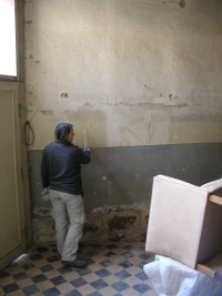 Stine steht vor einer alten brüchigen Lehmwand und entwirft